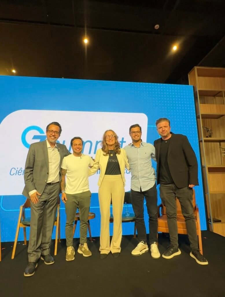 Cinco profissionais sorrindo em um palco com fundo azul.