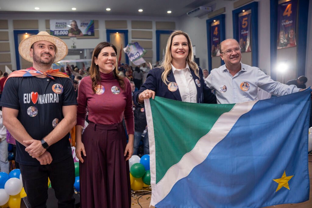 Quatro pessoas sorridentes segurando a bandeira de Mato Grosso do Sul.