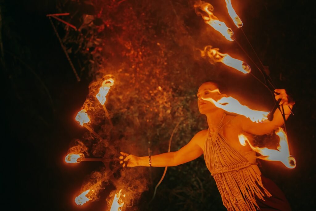 Mulher realizando performance artística com leques de fogo à noite.