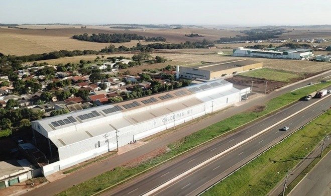 Vista aérea de galpão industrial com painéis solares na cobertura.