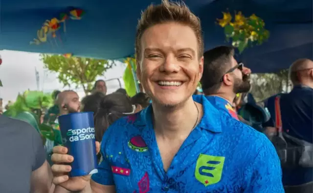 Michel Teló sorrindo e segurando um copo em evento.