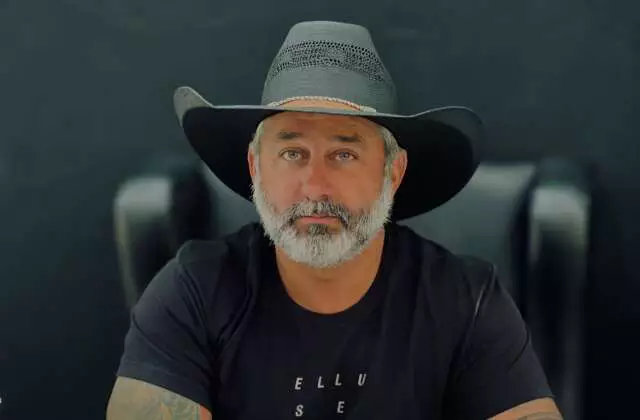Homem de barba grisalha usando chapéu de cowboy preto.