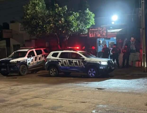 Duas viaturas da Polícia Militar estacionadas em rua à noite.