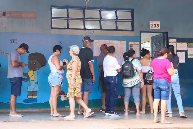 Pessoas em fila em frente a uma seção eleitoral.