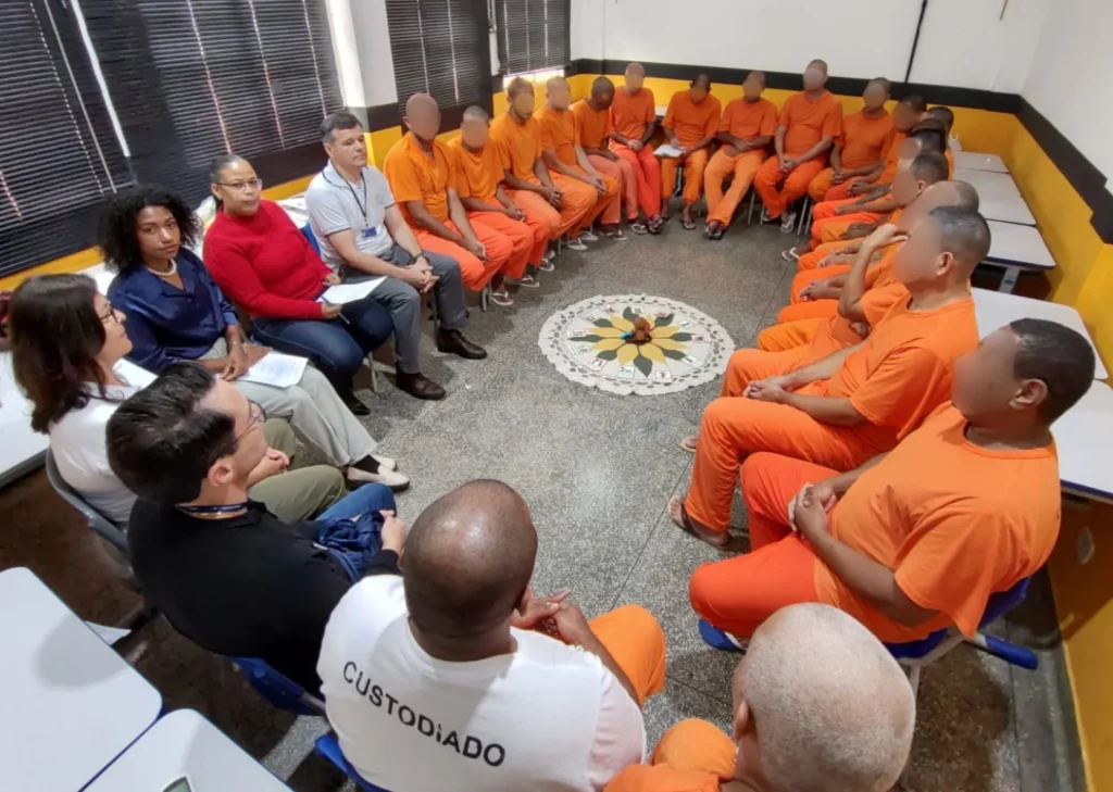 Detentos em uniformes laranja e facilitadores sentados em círculo.