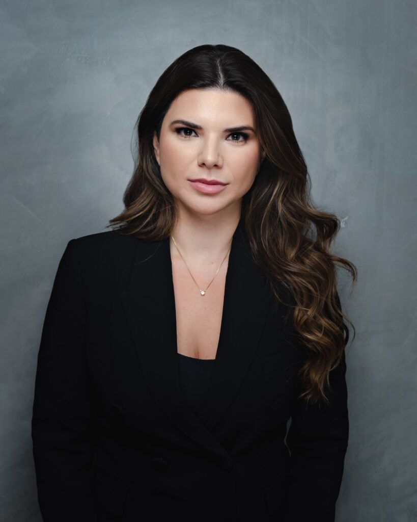 Mulher profissional de blazer preto em frente a fundo cinza.
