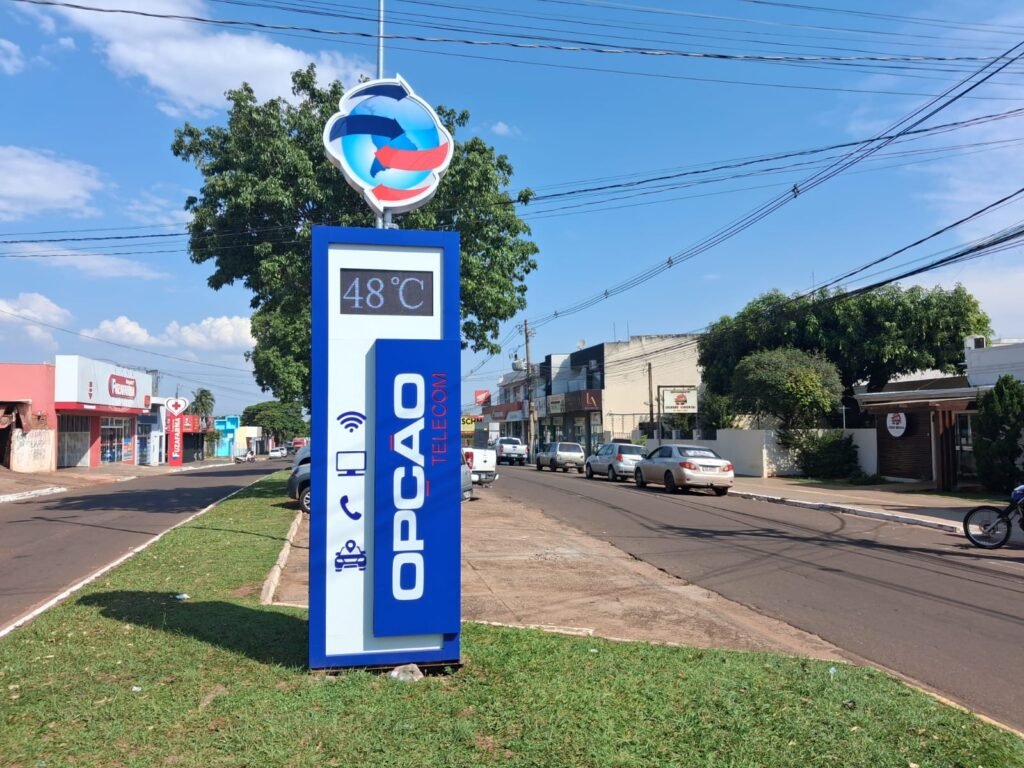 Totem da Opção Telecom marcando 48 graus em rua ensolarada.