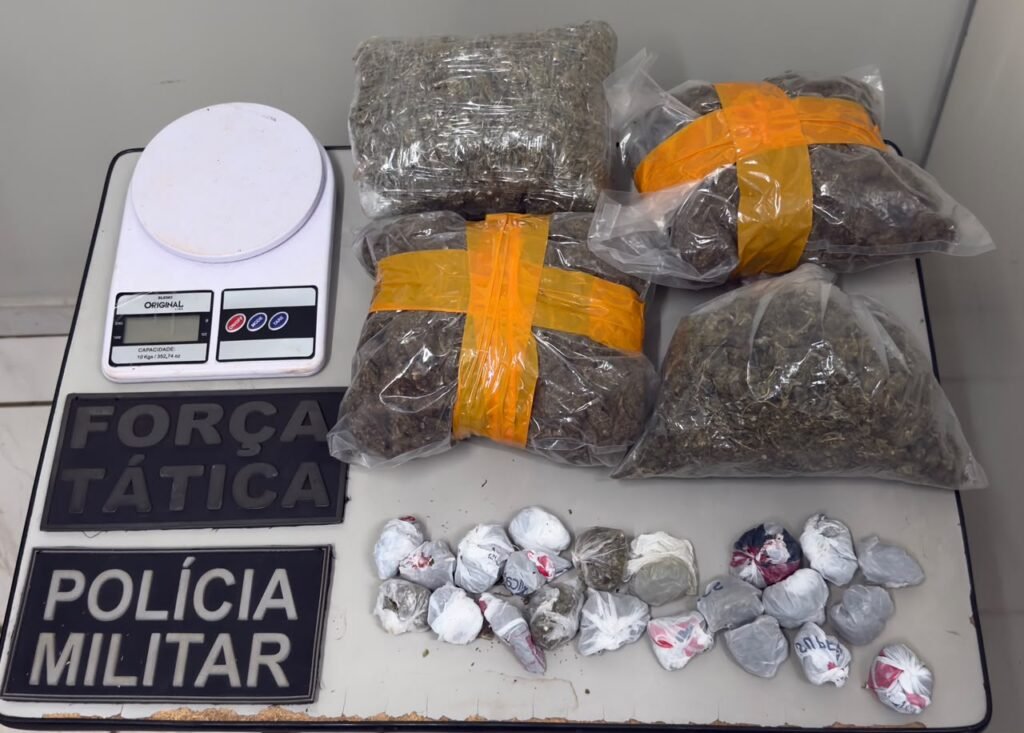 Drogas apreendidas, balança e insígnias da Polícia Militar sobre mesa.