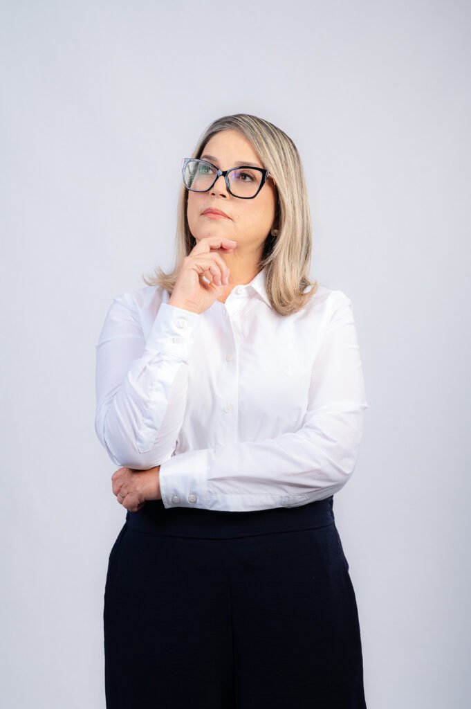 Mulher de óculos em pose pensativa sobre fundo branco.