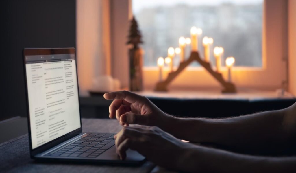 Pessoa usando laptop com decoração natalina iluminada ao fundo.