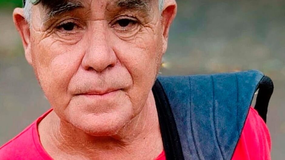 Homem idoso com expressão séria vestindo camiseta vermelha.