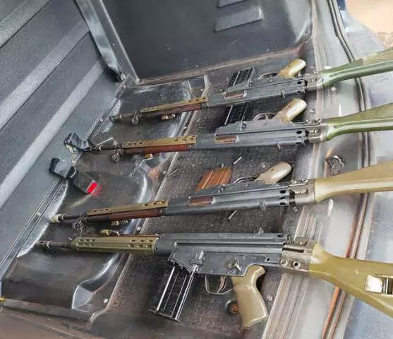 Quatro fuzis automáticos dispostos no porta-malas de um veículo.