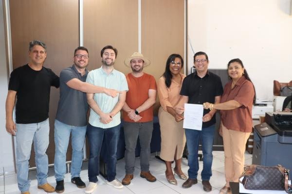 Grupo de sete pessoas sorrindo em um escritório com documento.
