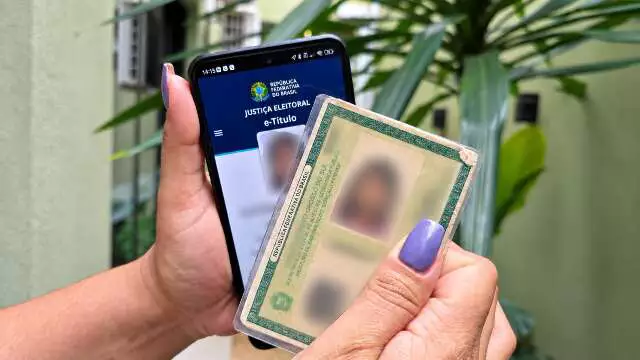Mãos segurando celular com e-Título e documento de identidade físico.