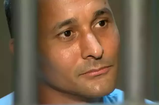 Homem atrás de grades olhando pensativo para o lado.