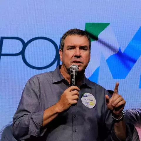 Homem falando ao microfone com o dedo indicador levantado.