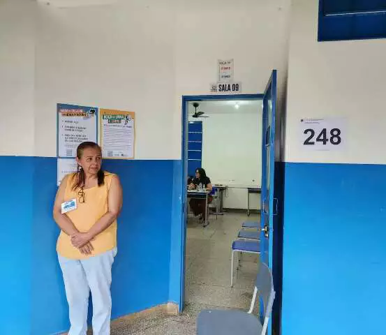 Mulher em frente a uma sala de aula identificada.