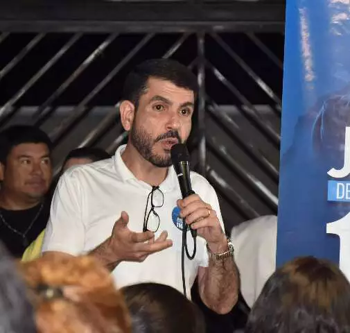 Homem de camisa branca discursando com microfone em evento.