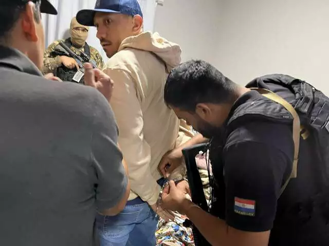 Policiais algemando um homem com boné azul em ambiente interno.