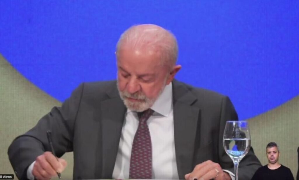 Presidente Lula assinando um documento oficial em uma mesa.