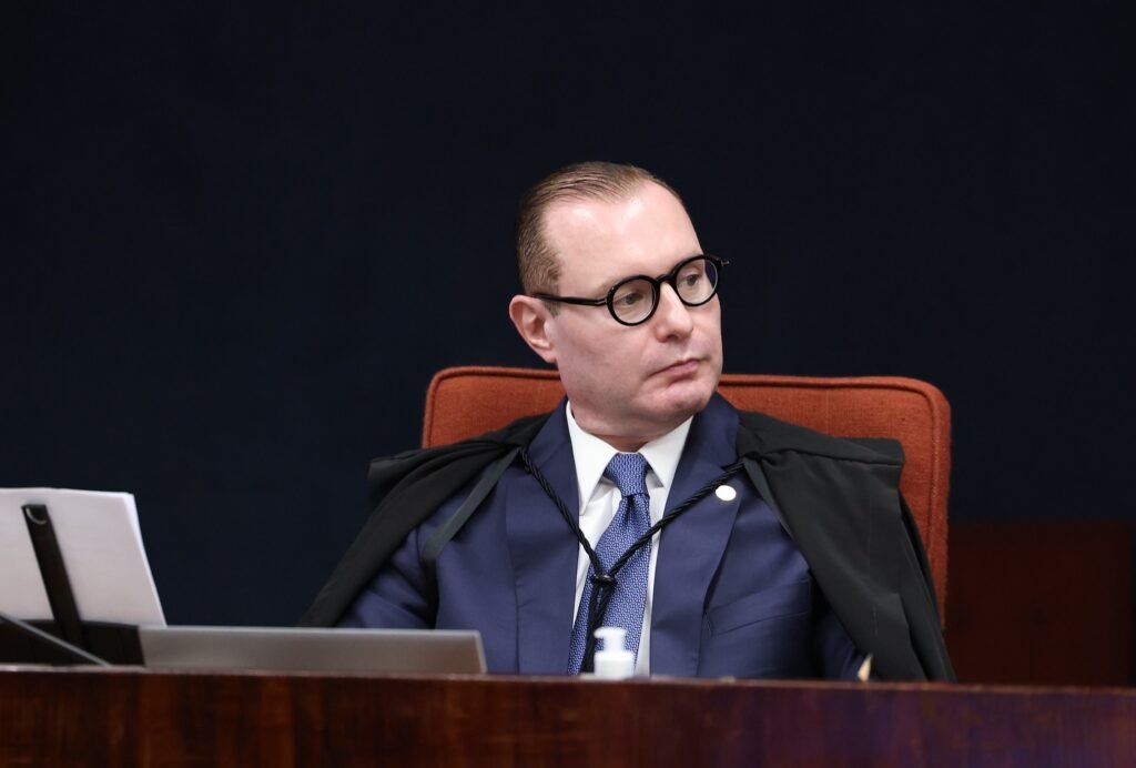 Homem de óculos e toga preta sentado em tribunal.