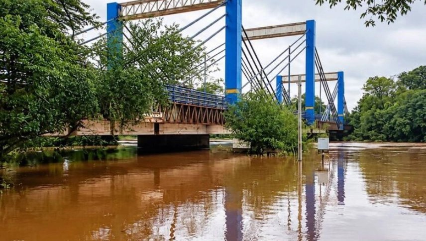 Ponte estaiada azul sobre rio com águas marrons e elevadas.