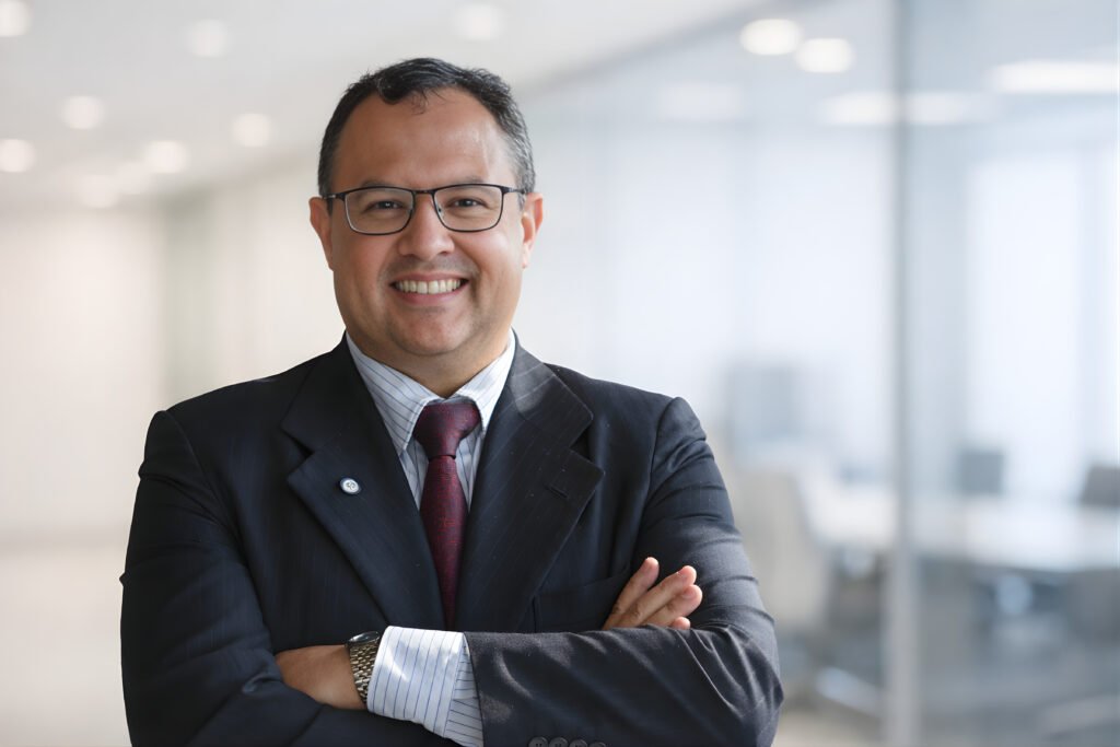 Executivo sorridente de óculos e terno em ambiente corporativo.