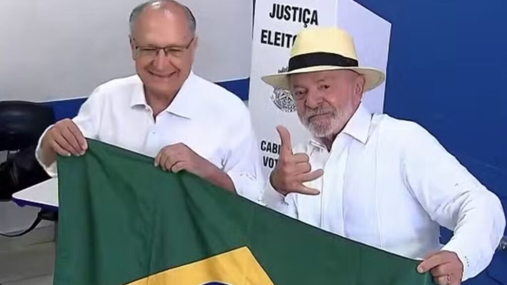 Lula e Alckmin sorridentes segurando a bandeira do Brasil.