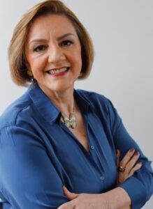 Mulher sorridente de camisa azul com braços cruzados.