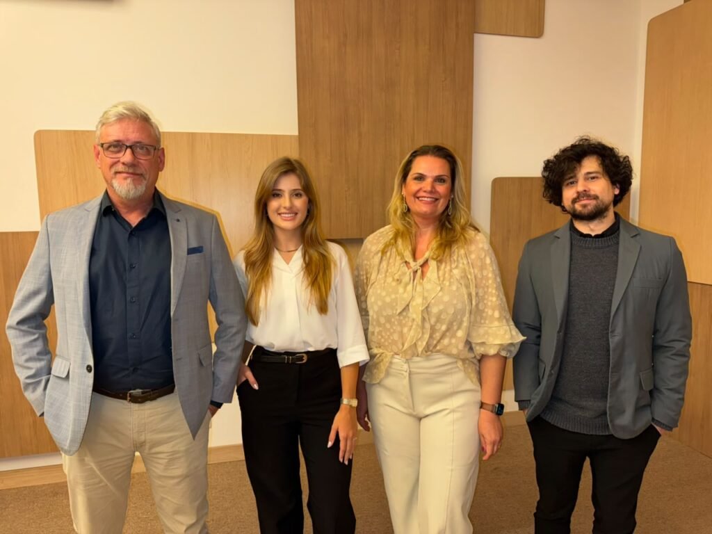 Quatro profissionais sorrindo em pé em um escritório moderno.