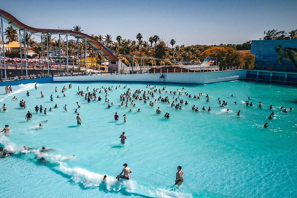 Piscina de ondas lotada em um parque aquático ensolarado.