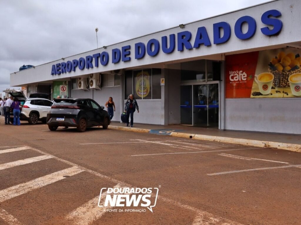 Fachada do Aeroporto de Dourados com carros e pessoas.