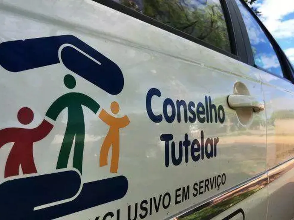 Logotipo do Conselho Tutelar na lateral de um carro branco.