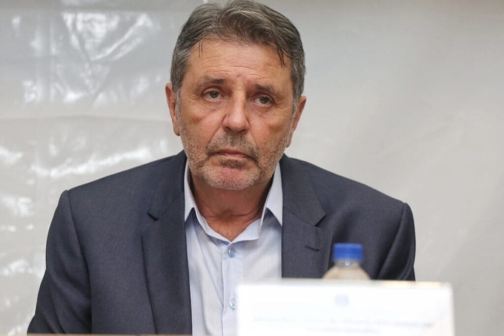 Homem de terno e camisa azul com expressão séria.