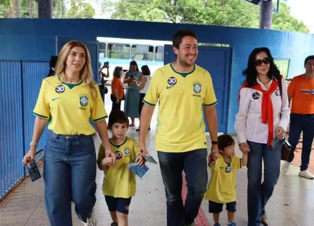 Família com camisas da seleção brasileira caminhando de mãos dadas.