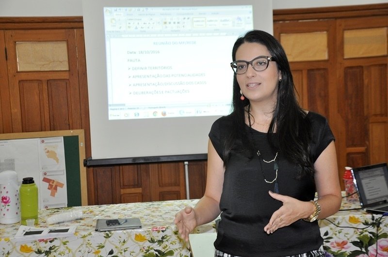 Mulher palestrando com tela de projeção ao fundo.