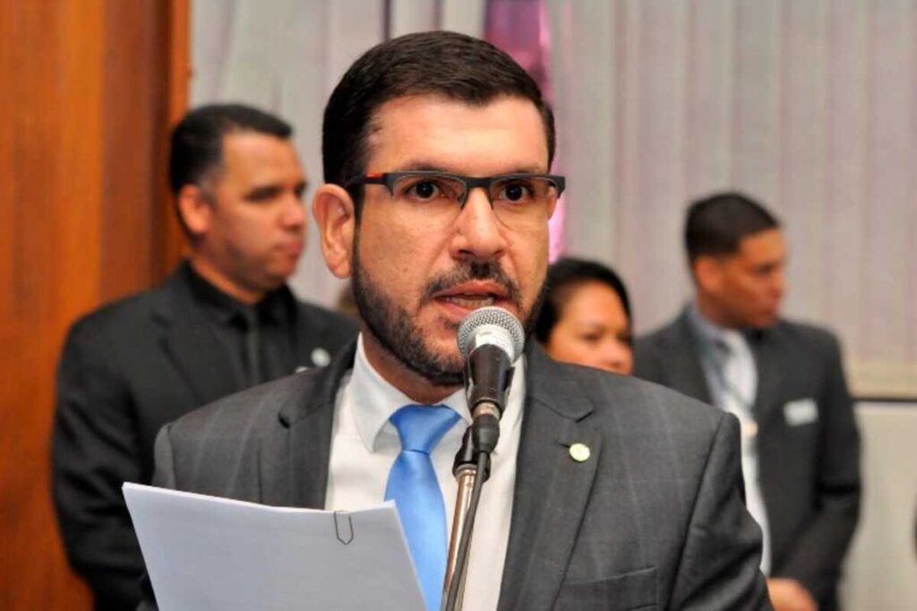Homem de terno e óculos falando em um microfone.