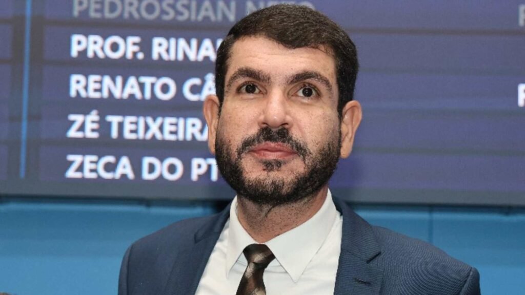 Homem de terno e barba em frente a painel eletrônico.