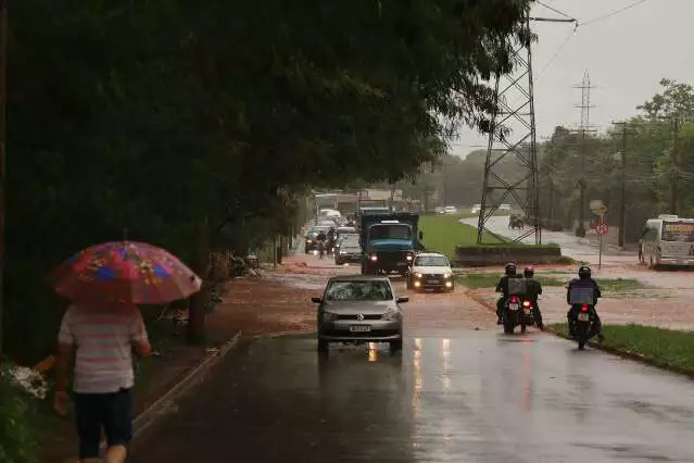 Trânsito em rua alagada sob chuva com pedestre e veículos.