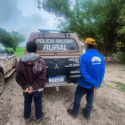 Dois homens de costas diante de uma viatura policial rural.