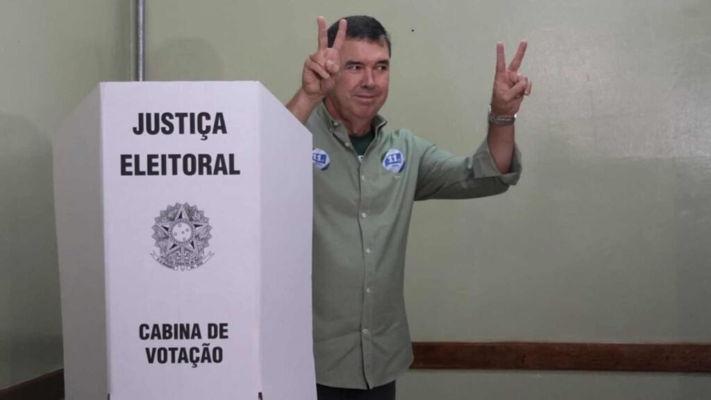 Homem faz sinal de vitória em cabine de votação brasileira.