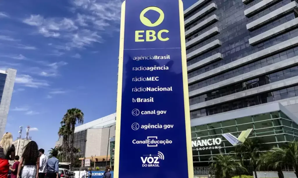 Totem azul da EBC em frente a um edifício moderno.