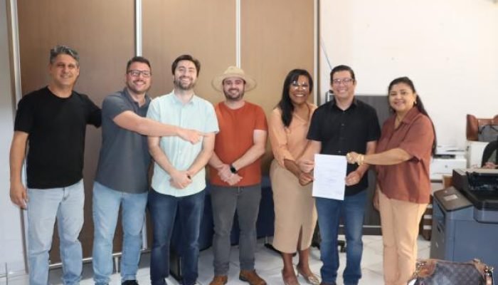 Grupo de sete pessoas sorrindo em um escritório com documento.
