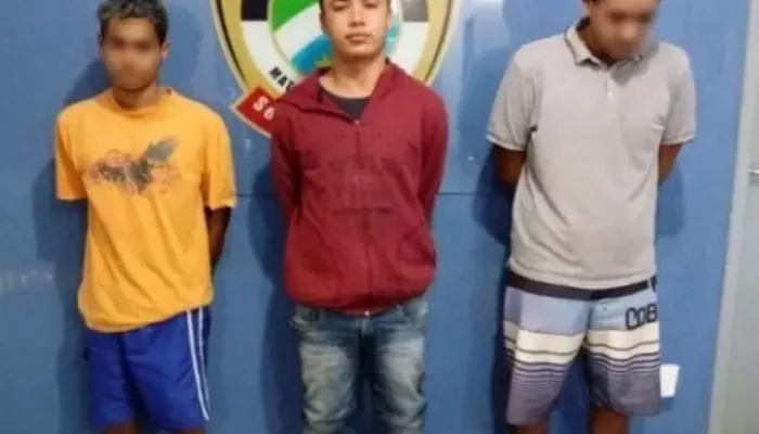 Três homens detidos em frente a um escudo policial.