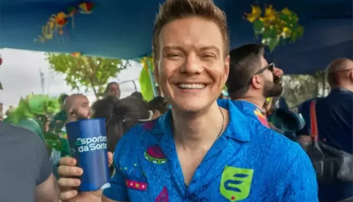 Michel Teló sorrindo e segurando um copo em evento.