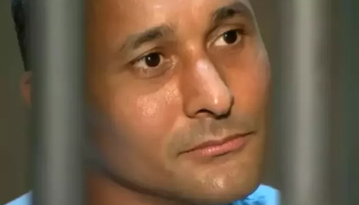Homem atrás de grades olhando pensativo para o lado.