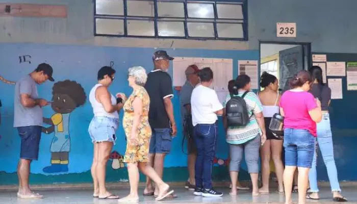 Pessoas em fila em frente a uma seção eleitoral.