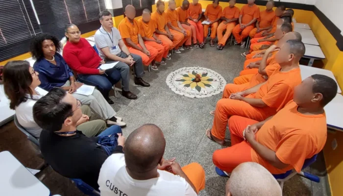 Detentos em uniformes laranja e facilitadores sentados em círculo.