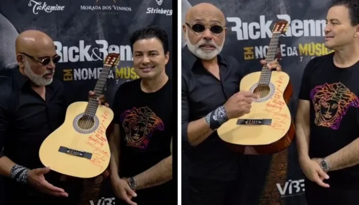 Rick e Renner segurando um violão autografado em um evento.