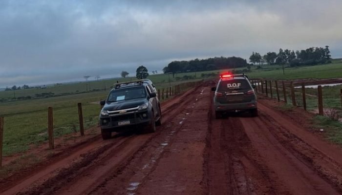 Viatura policial e caminhonete em estrada de terra lamacenta.